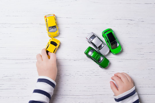 Child hands playing with miniature toy cars, wooden background, top view