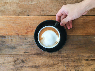 Cup of cappucino / latte hot coffee with hand holding cup saucer on wooden background