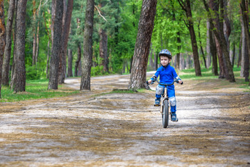 Happy cute blond kid boy having fun his first bike on sunny summer day, outdoors.  child making sports. Active leisure for children.  wear safety helmet.  is smiling and cicling.