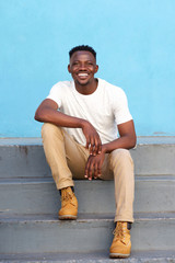 stylish young man sitting on steps and smiling