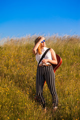 Teenage girl walking through a grassy field carrying a guitar. Outdoors. Summer.