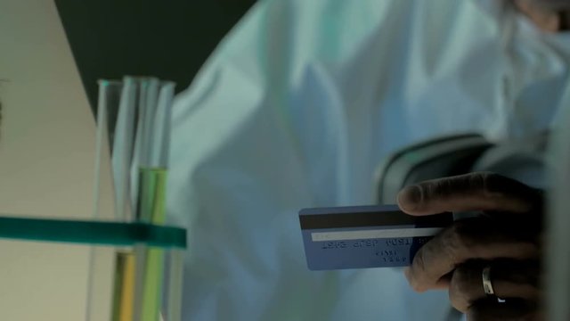 Close look of elderly scientist with laptop and credit or debit card. Shot can be used to demonstrate online shopping of professional buyers in industry. People using e-commerce in their work