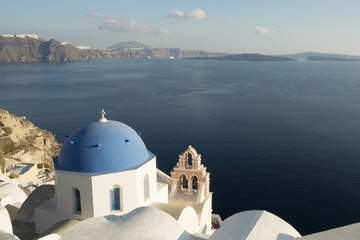 A famous blue domed church at Oia village, Santorini with the volcano's caldera in the background