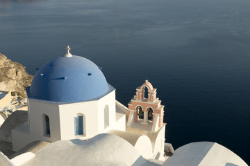 A famous blue domed church at Oia village, Santorini with the volcano's caldera in the background