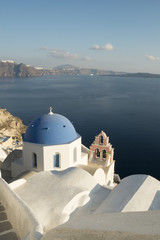 Fototapeta na wymiar A famous blue domed church at Oia village, Santorini with the volcano's caldera in the background