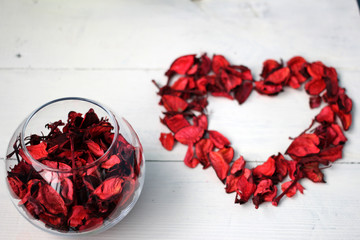 Красное сердце из лепестков сухих цветов (роз) на белом фоне и ваза с лепестками