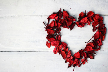 Красное сердце из лепестков сухих цветов (роз) на белом фоне