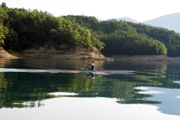 Fototapeta na wymiar A Young single scull rowing competitor paddles on the tranquil lake