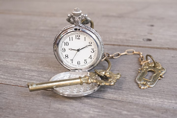 Vintage Pocket Watch, with vintage key and lock in bronze. Soft focus on pocket watch's face. isolated on wood