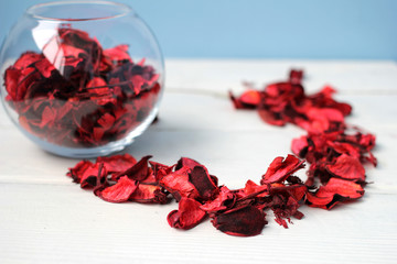 Лепестки роз в стеклянной круглой вазе и на белом столе
