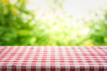 Red checkered tablecloth texture top view with abstract green from garden background.