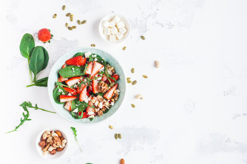 Fototapeta na wymiar Strawberry salad. Spinach leaves, sliced strawberries, nuts, feta cheese on white background. Healthy food concept. Fat lay, top view