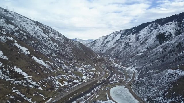 Aerial mountain canyon valley highway traffic. Wasatch Mountain Range central Utah. Highway in deep canyon valley traffic travel. Winter snow. Landscape scenic and rugged. Drone aerial flight.