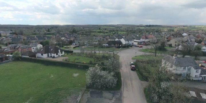 Aerial view of UK middle class houses in small village or town in the countryside. Top view above houses surrounded by green lawns and farmland.