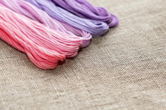 Set for embroidery. Embroidery thread shades of violet and pink color on linen homespun cloth. Coloring and processing photos. Shallow depth of field.