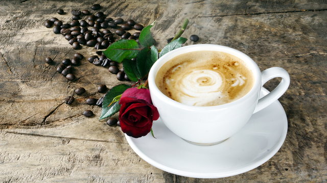 Cappuccino coffee with roses. A cup of latte, cappuccino or espresso coffee with milk put on a wood table with dark roasting coffee beans. Drawing the foam milk on top.