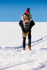 Couple playing in snow. Man giving woman piggyback ride on winter vacation.