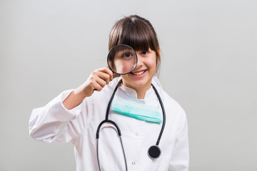 Beautiful little doctor looking through loupe.