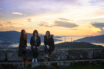 Tres mujeres jóvenes delante del atardecer sobre la Ría de Vigo