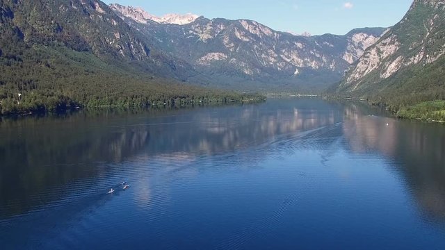 Flight above amazing Bohinj Lake in the morning. People are training in rowing. Blue deep water and Julian Alps mountains. Triglav National Park, Slovenia, Europe.