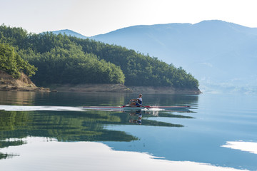 A Young single scull rowing competitor paddles on the tranquil lake