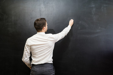 Man in suit pointing something on chalkboard,back view,isolated.Copyspace blank.Teacher writing on...