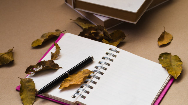Pen and notebook with dried leaves on brown paper