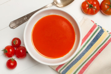 Sopa crema de tomates en cuenco blanco con cuchara de metal antigua sobre mesa blanca de madera. Vista superior