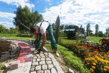 Handwerker verlegt Pflastersteine in einer Gartenanlage  © reichdernatur