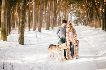 Outdoor happy couple in love posing with dog in cold winter weather. Young boy and girl having fun outdoor. Boho