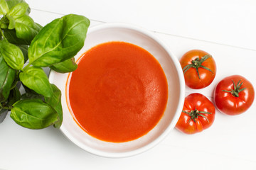 Sopa crema de tomate en cuenco blanco con albahaca sobre fondo blanco aislado. Vista superior