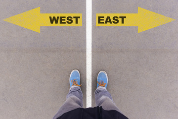 West and East text arrows on asphalt ground, feet and shoes on f