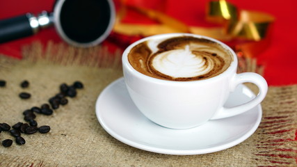Cappuccino coffee and gold ribbons. A cup of latte, cappuccino or espresso coffee with milk on red background with dark roasting coffee beans. Drawing the foam milk on top.