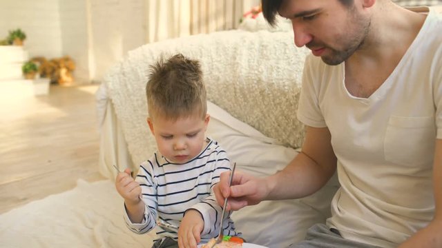 Little adorable boy celebrating his birthday with young father eat cake in bedroom