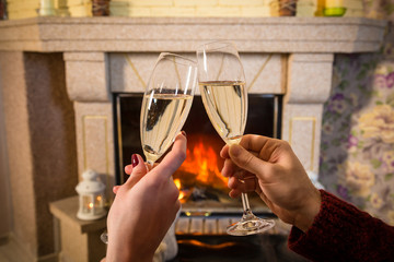 Couple's hands with glass of champagne near fireplace