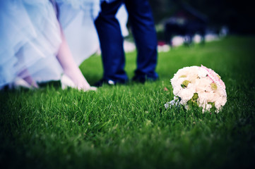 Naklejka premium Young couple standing on the grass. In the foreground is a bridal bouquet