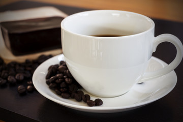 Hot coffee in a white cup and chocolate cake shot on a dark background.