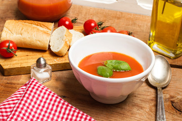 Sopa crema de tomate en cuenco blanco con albahaca sobre mesa de madera. Vista superior