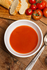 Sopa de tomate en cuenco blanco y cuchara de metal sobre mesa de madera. Vista superior