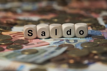 saldo - Holzwürfel mit Buchstaben im Hintergrund mit Geld, Geldscheine