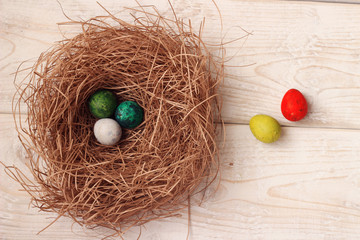 Colorful Easter eggs in the nest of a bird on a wooden board.
