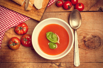 Sopa crema de tomate en cuenco blanco con albahaca sobre mesa de madera. Vista superior