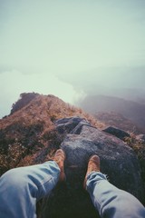 Man wears boots and jean sitting on top of the mountain.