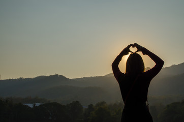 Silhouette of Asia Woman making Sign of Heart with the Sunlight when Sunset.