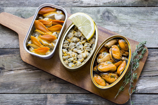 
Cans of preserves with clams, cockles and mussels on a rustic table