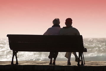 Silhouette seniors couple waiting for colourfull sunset on the bench near ocean - Powered by Adobe