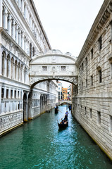 Fototapeta premium Couple in Venice float under the Bridge of Sighs by gondola boat. The enclosed bridge connects the New Prison to the interrogation rooms in the Doge's Palace. 