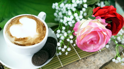 Cappuccino coffee and chocolate cookies. A cup of latte, cappuccino or espresso coffee with milk put on a wood table with dark roasting coffee beans and cookies. Drawing the foam milk on top.