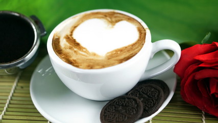 Cappuccino coffee and chocolate cookies. A cup of latte, cappuccino or espresso coffee with milk put on a wood table with dark roasting coffee beans and cookies. Drawing the foam milk on top.