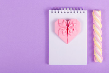 Open notebook, heart origami and marshmallow stick on a purple background. St. Valentine's Day. Copy space